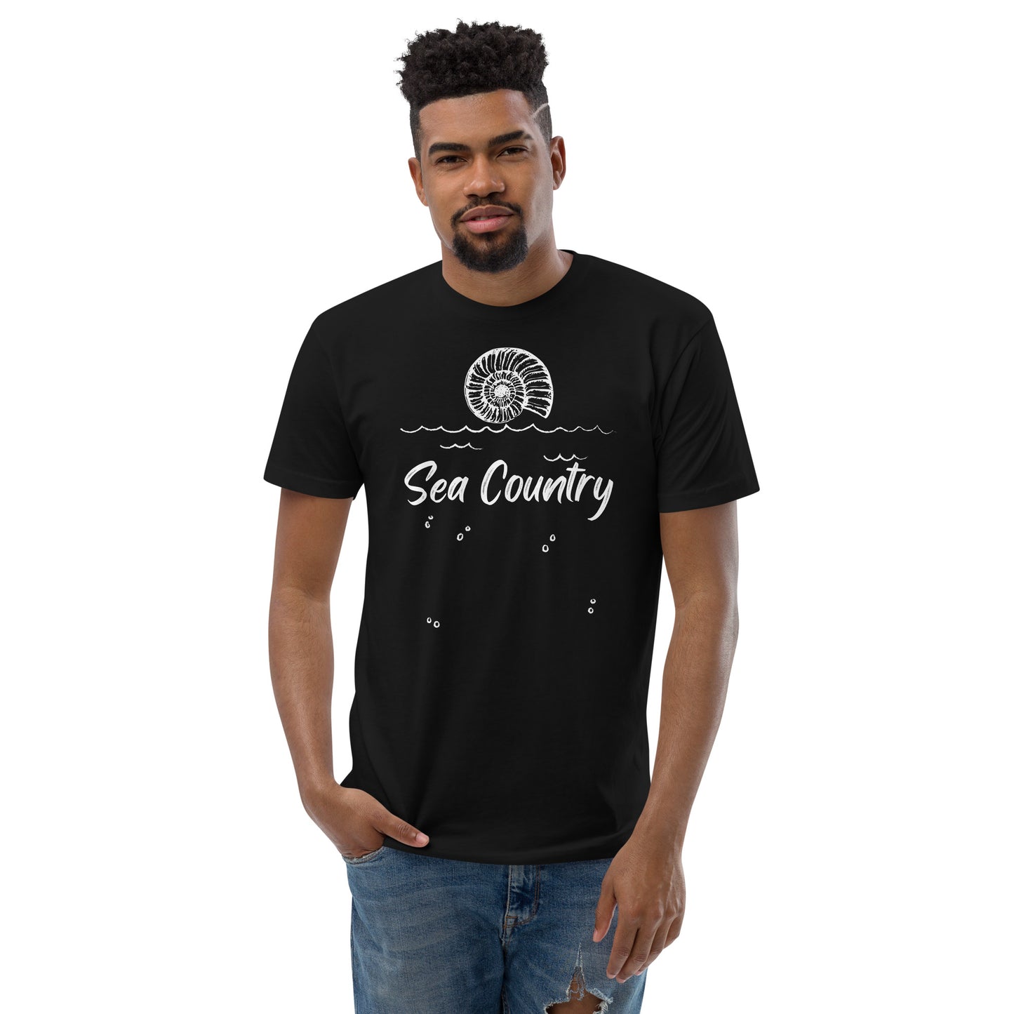 Black tshirt with large shell sitting over waves and the words Sea Country printed in white on black tshirt. Model wearing denim jeans.