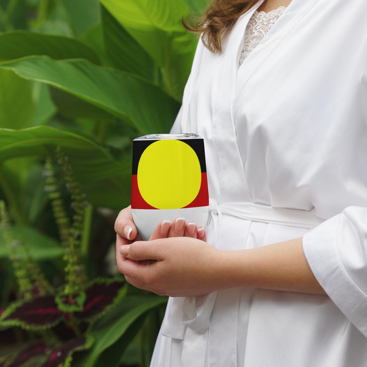 Stainless Steel; wine tumbler in white. Featuring Large Aboriginal flag. Front View. Being cupped in two hands by woman in white shirt.