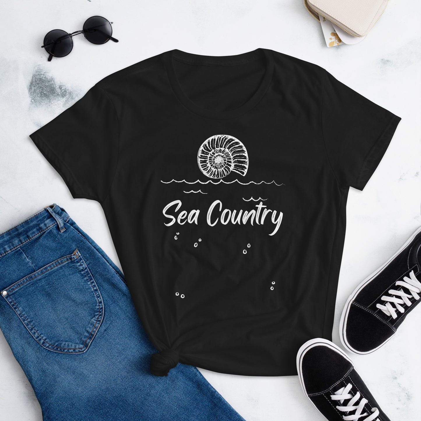 Black T-Shirt with shell pictured on top and the words Sea Country printed underneath. Pictured with denim jeans and black sneakers.