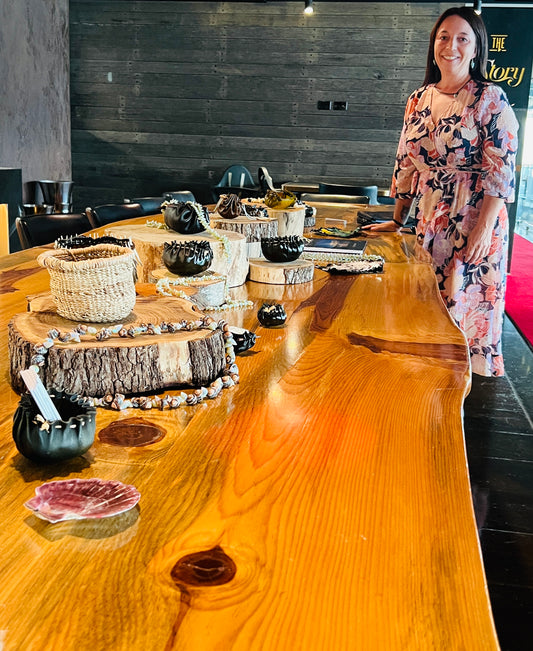 Lady in pink floral dress standing at a long timber table.  Cultural objects line the table as a lovely display.